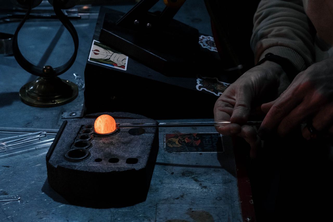 Close-up of a craftsman shaping glass over a flame in a dimly-lit workshop.