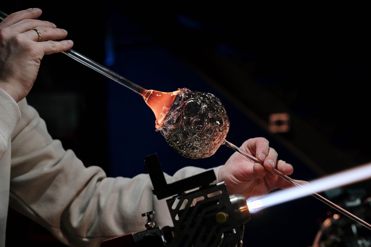 Close-up of a craftsman skillfully working with glass and flame in a dimly lit studio.